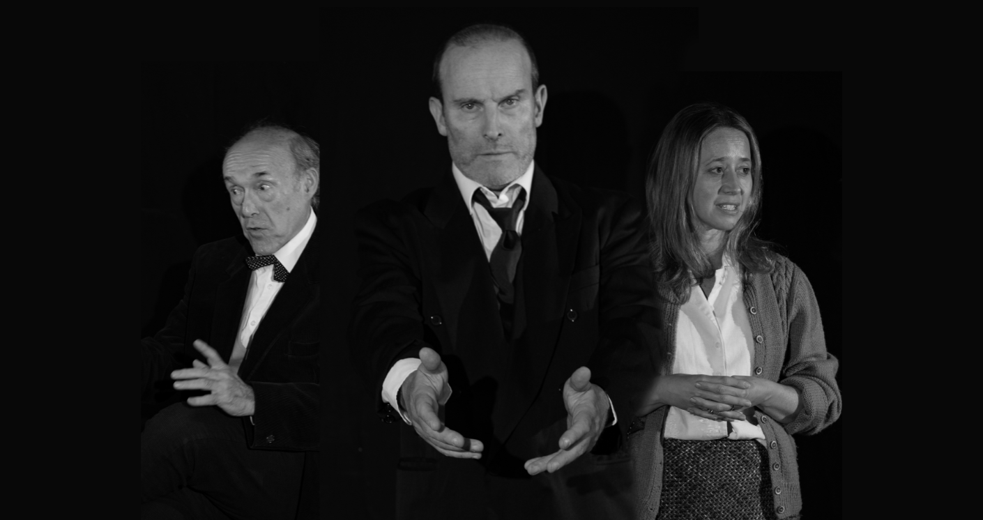 A middle aged man in the centre of the image holds his hands out, looking down the camera. On his left, an older man seems in the middle of a conversation. On his right, a younger woman worriedly clasps her hands and looks off into space.